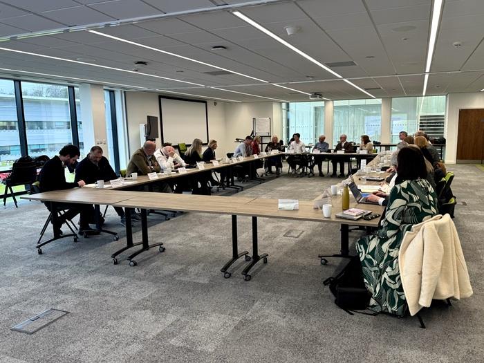 A group of people seated at a large table in a modern meeting room, participating in a roundtable discussion.
