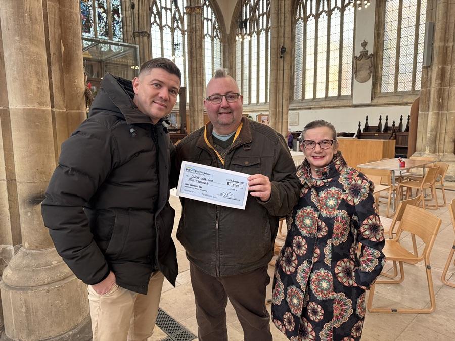 Three people stand indoors, smiling and holding a cheque inside Hull Minster.